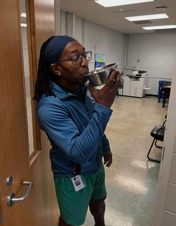 Man drinking from a metal bowl, showcasing creative sippers choosing to drink from anything but a cup in an office setting.