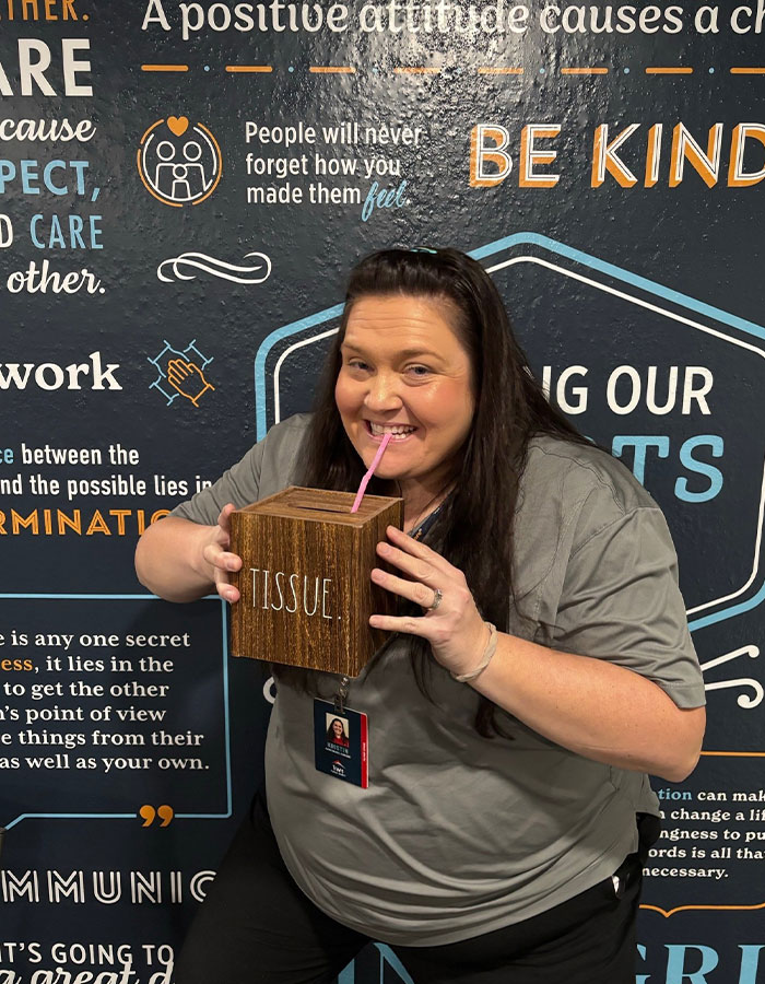 Woman drinking creatively from a tissue box using a pink straw against a motivational wall background, showcasing unique sippers.
