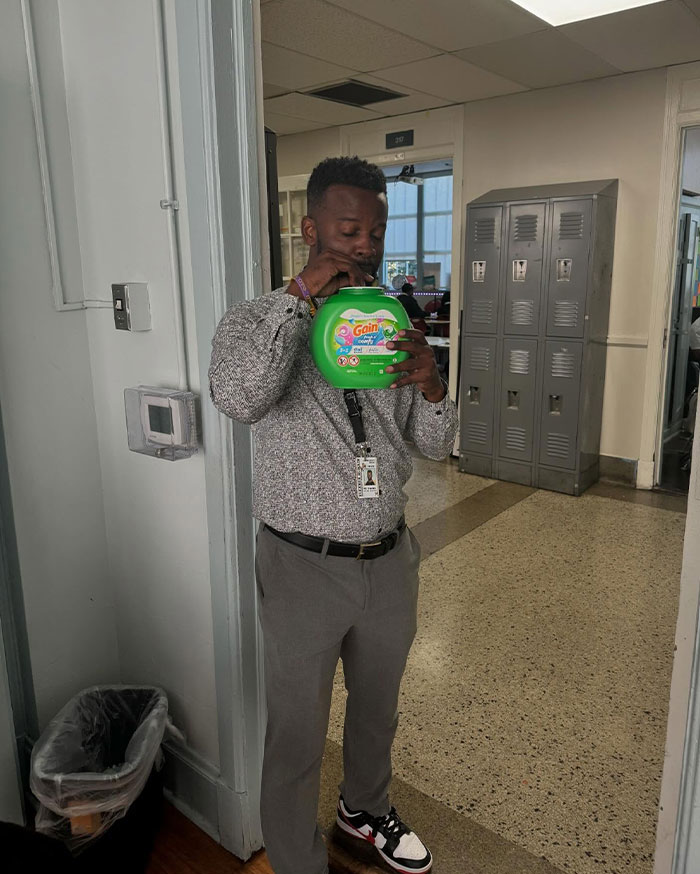 Man creatively sipping from a laundry detergent container in a hallway with lockers, showcasing unique sippers.
