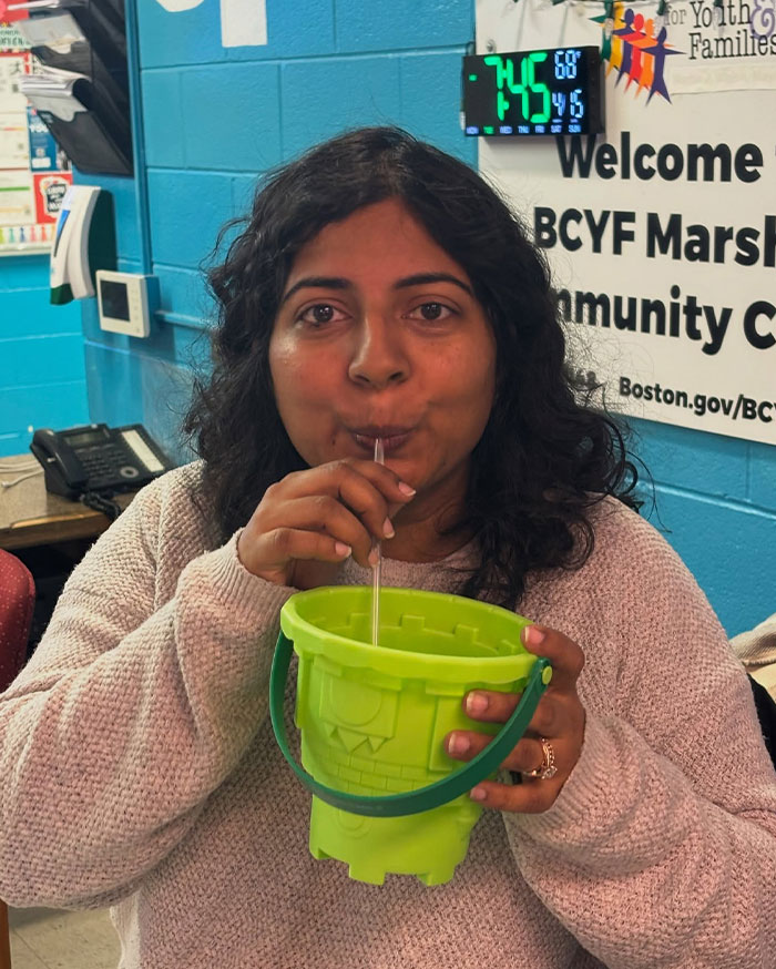 Woman sipping drink through a straw from a bright green bucket, showcasing creative sippers choosing to drink from anything but a cup.