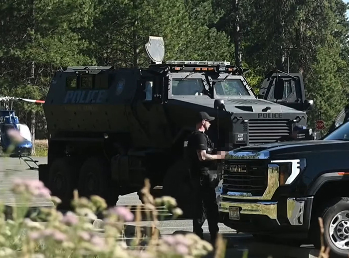 Police armored vehicle and officer at a wooded scene related to Idaho teen sniper shooting firefighters investigation.