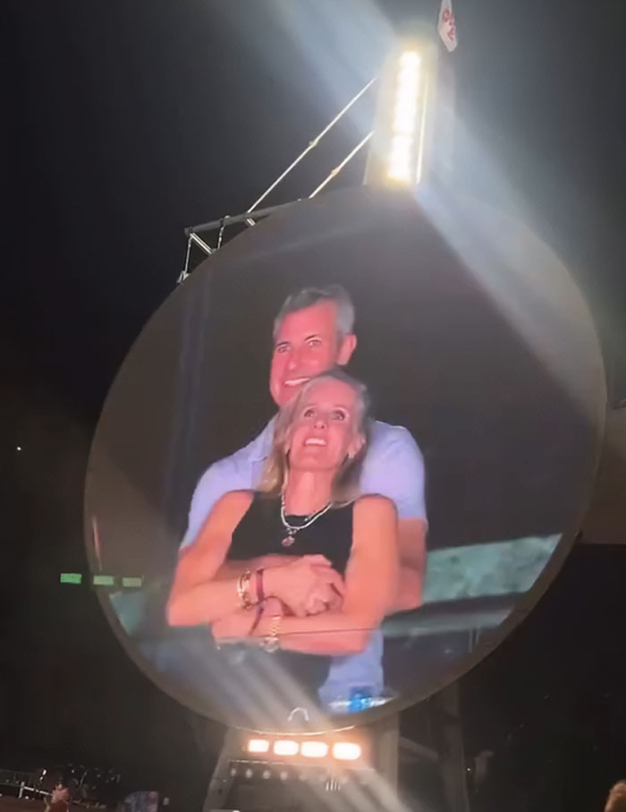 Couple embracing on a Coldplay kiss cam at night, with Astronomer interim CEO controversy in the background. Couple embracing on a Coldplay kiss cam at night, with Astronomer interim CEO controversy in the background.