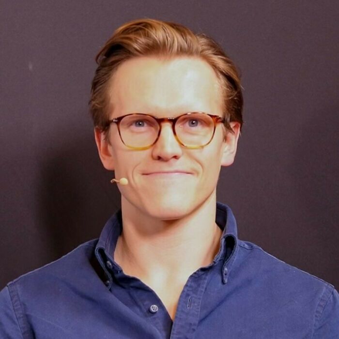 Young man wearing glasses and a blue shirt speaking with a microphone, related to astronomer interim CEO response. Young man wearing glasses and a blue shirt speaking with a microphone, related to astronomer interim CEO response.