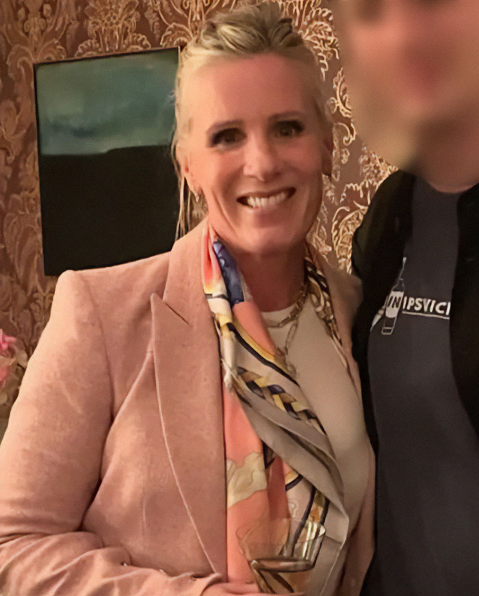 Coldplay HR executive smiling indoors, wearing a pink blazer and colorful scarf, highlighted by friends from elite sorority days.