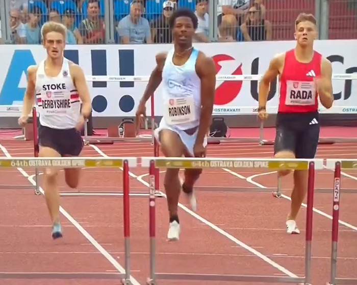 Sprinter Robinson competing in a hurdles race on a professional track with spectators watching in the background. Sprinter Robinson competing in a hurdles race on a professional track with spectators watching in the background.