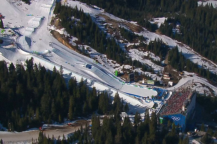 Olympic medalist skier competing on a snowy mountain slope during an event with a large crowd and Olympic rings visible. - 8