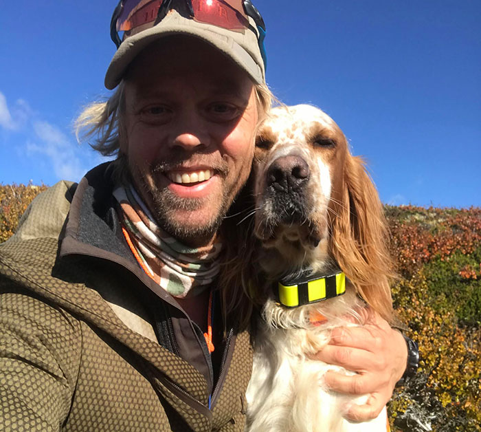 Olympic medalist skier smiling outdoors with his dog, enjoying nature on a sunny day. - 5