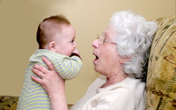 Elderly woman holding baby with gold stud earrings after unlicensed ear piercing during family visit.