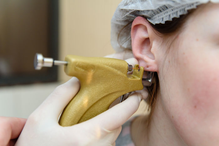 Close-up of unlicensed ear piercing with a gold stud being inserted into a woman&rsquo;s ear during a baby visit.