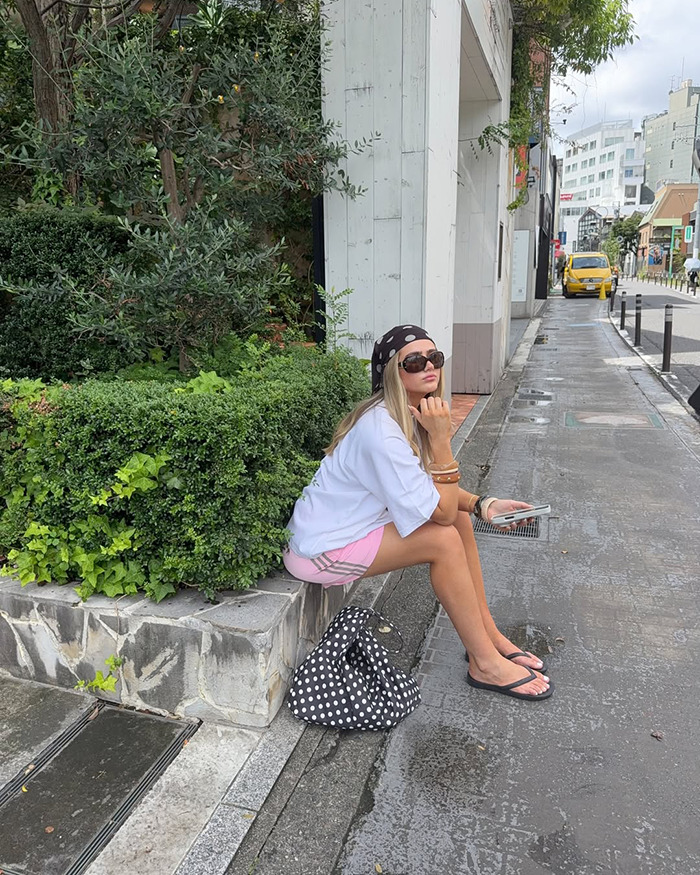 Australian influencer sitting on a city sidewalk in Japan, wearing sunglasses and casual summer clothes during trip. - 5