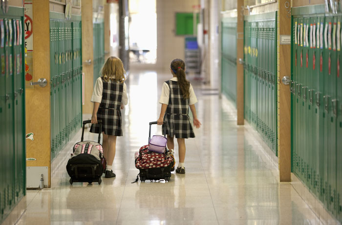 Two schoolgirls in uniforms walking down a hallway with rolling backpacks, representing average IQ in the USA 2025.