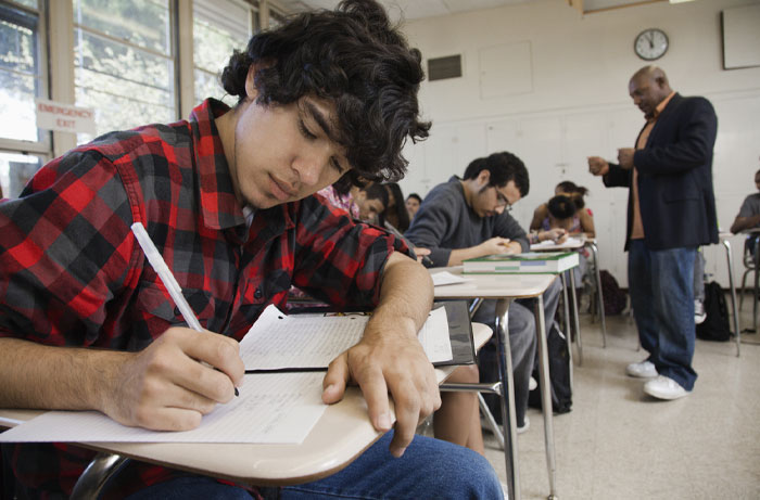 Student in classroom writing on paper during test, illustrating average IQ in the USA with state leaders and laggards.