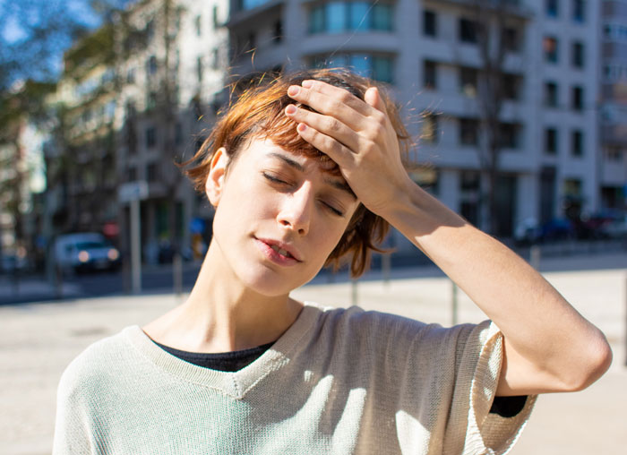 Young woman outdoors in city shading forehead from heat, highlighting extreme heat warnings in 18 states for Americans. - 5