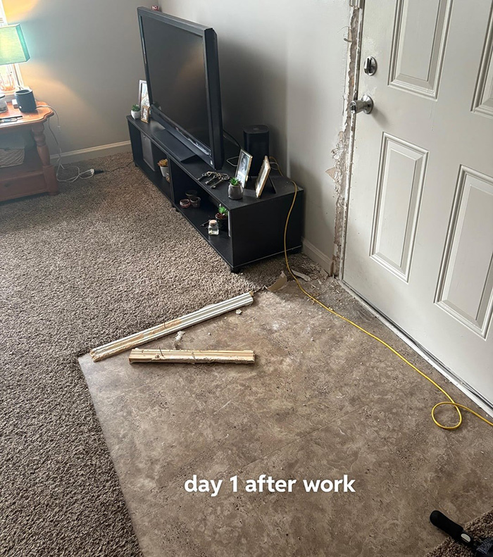 Living room floor damaged by dog, showing removed carpet and exposed area near door with wood pieces scattered.