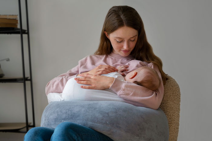 Mother cradling infant closely while seated, showing tender moment between parent and baby indoors.