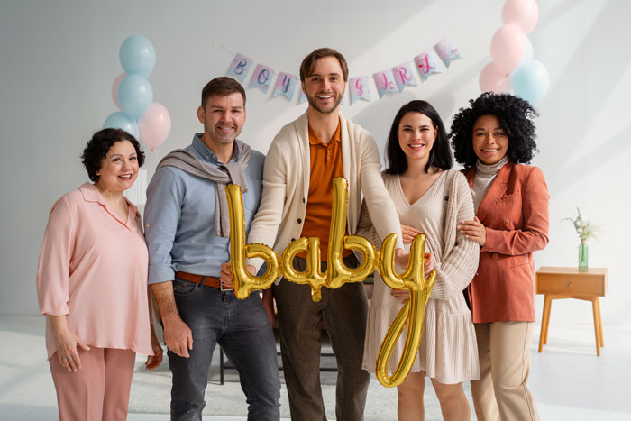 Group of friends holding golden baby balloons at a man’s baby shower, with pastel decorations in the background. - 4