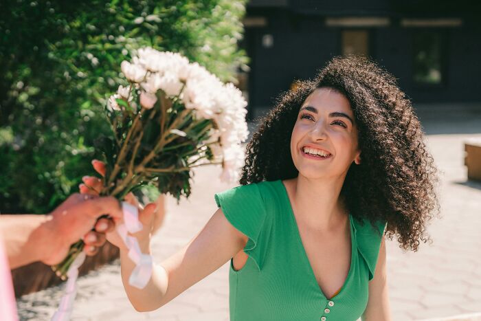 A smiling woman in a green dress receiving a bouquet, representing bare minimum or princess treatment concepts.