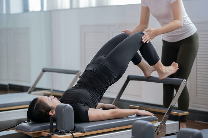 Woman receiving Pilates reformer exercise assistance from instructor, illustrating bare minimum or princess treatment options.