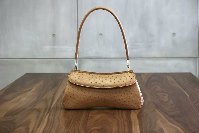 Light brown ostrich leather handbag resting on a wooden table, showcasing minimalist and princess treatment style.