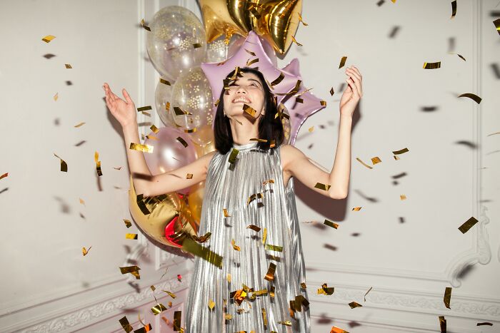 Young woman in a silver dress enjoying princess treatment with confetti and star-shaped balloons in a festive setting.