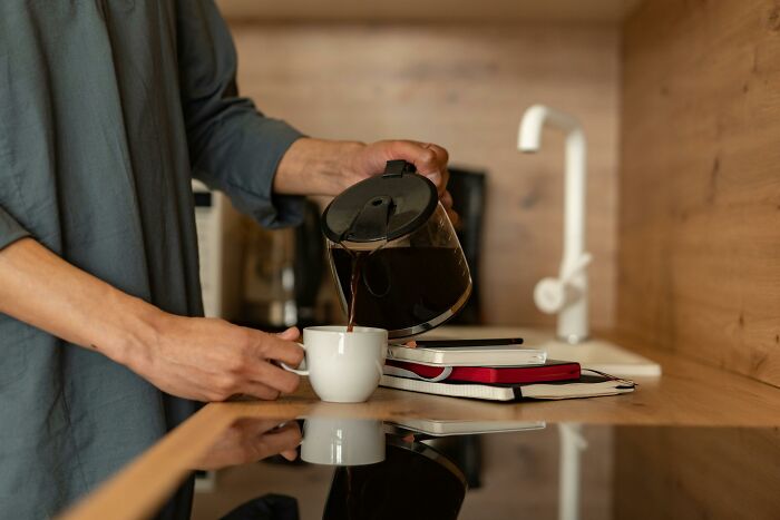 Person pouring coffee into a cup on a kitchen counter next to notebooks, illustrating bare minimum or princess treatment choices.