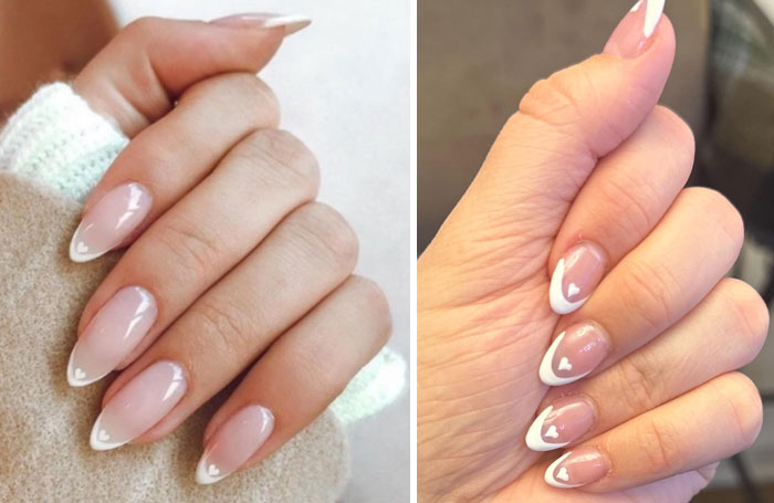 Close-up of hands with glossy n**e French tip nails featuring small white heart designs, showcasing a salon glow-up style.