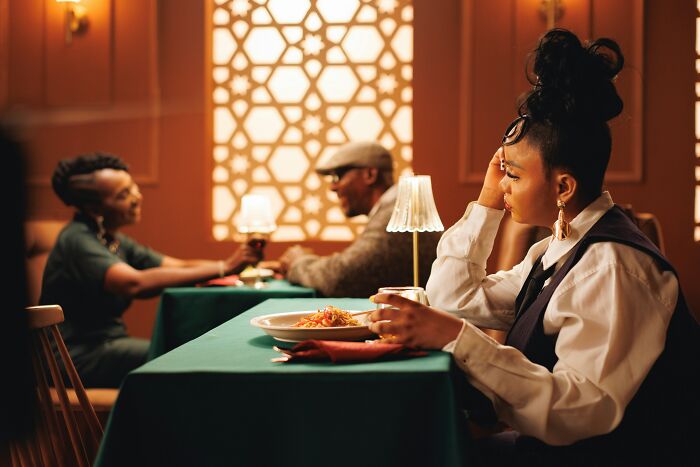 Woman looking upset and holding a drink at a restaurant table symbolizes red flag behaviors in romantic settings. - 21