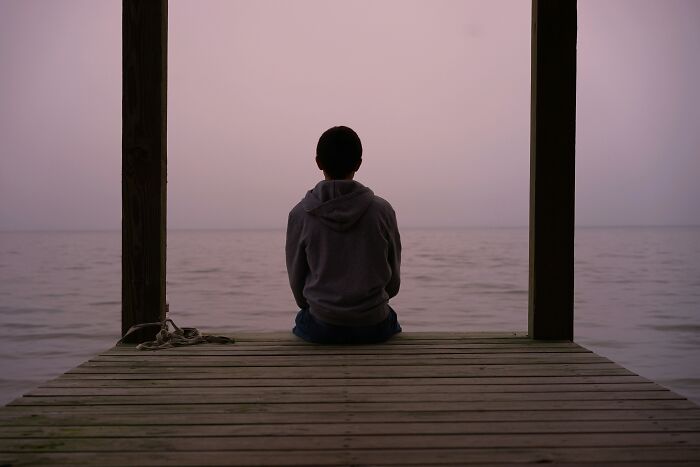 Person sitting alone on a dock overlooking calm water at dusk, reflecting on the benefits of night shift work. - 7
