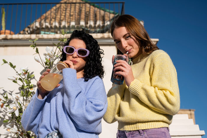 Two women enjoying drinks outside on a sunny day, highlighting a wannabe influencer and friendship conflict.