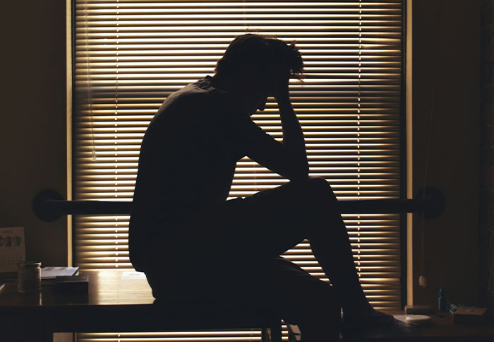 Silhouette of a man sitting with head in hand, reflecting on best friend saw girlfriend another man situation.
