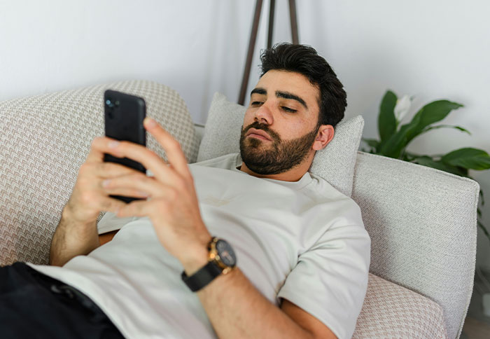 Man checking phone lying on couch, appearing serious, related to best friend saw girlfriend another man check email topic.