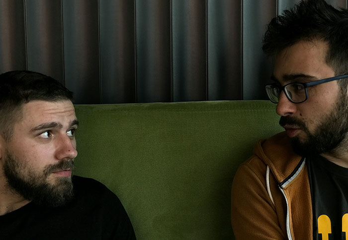 Two men sitting on a green couch looking at each other, conveying tension related to best friend saw girlfriend another man.