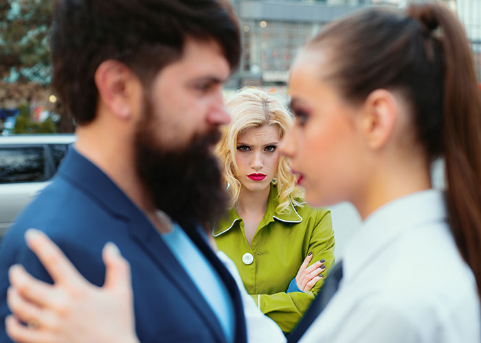 Blonde woman in green coat looks upset while couple in foreground embraces, illustrating life cheat codes concept. - 18