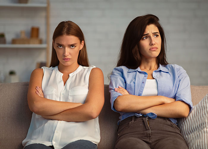 Two women sitting on a couch with arms crossed, showing frustration and tension, related to life cheat codes advice. - 39