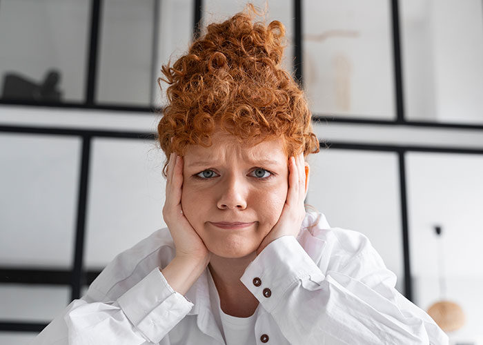 Young woman with curly red hair looking frustrated, holding her face, illustrating life cheat codes concept. - 20