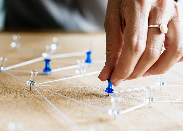 Hand placing a blue pushpin on a corkboard connected with string, illustrating life cheat codes concept. - 37