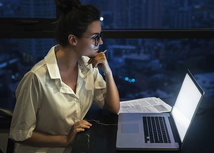 Woman wearing glasses working on laptop late at night, discovering useful life cheat codes for easier living. - 41