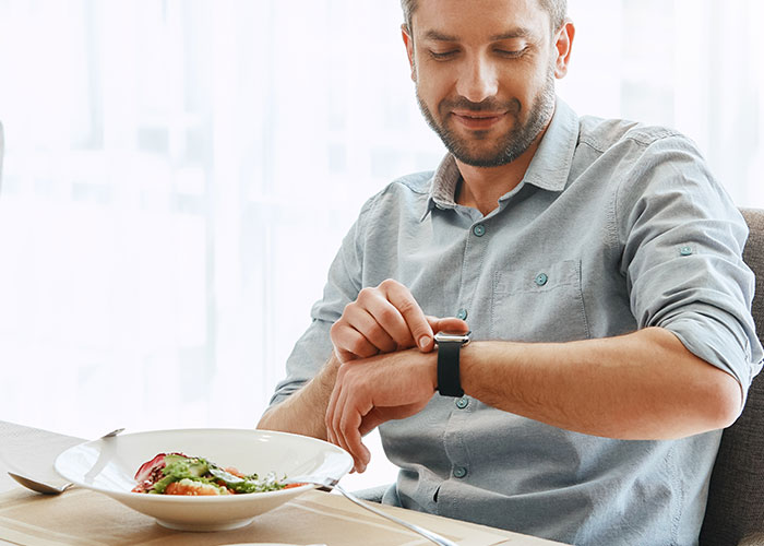 Man sitting at table with healthy food checking smartwatch, illustrating life cheat codes for better living. - 42