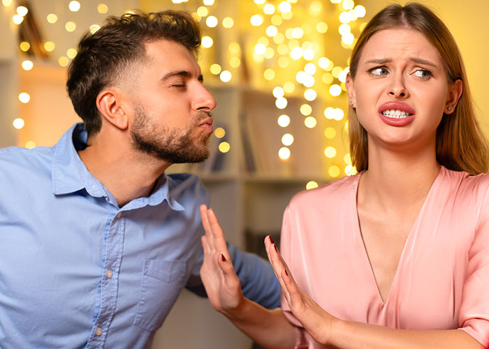 Man in blue shirt leaning in for a kiss while woman in pink blouse pushes him away, illustrating life cheat codes concept. - 3
