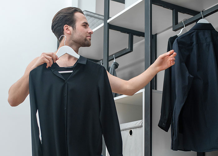 Man choosing between two black shirts in closet, illustrating life cheat codes for easier daily decisions. - 19