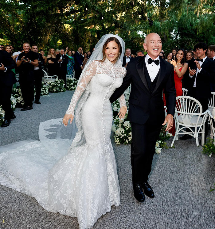 Sydney Sweeney in a white wedding dress with Jeff Bezos in a tuxedo at an outdoor event with guests applauding. Sydney Sweeney in a white wedding dress with Jeff Bezos in a tuxedo at an outdoor event with guests applauding.