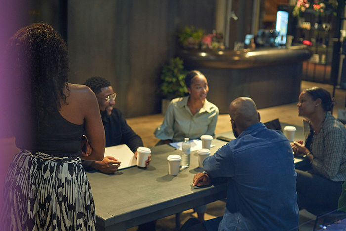 Group of young adults having a serious discussion indoors, illustrating tension about a man&rsquo;s brother and longtime girlfriend conflict.
