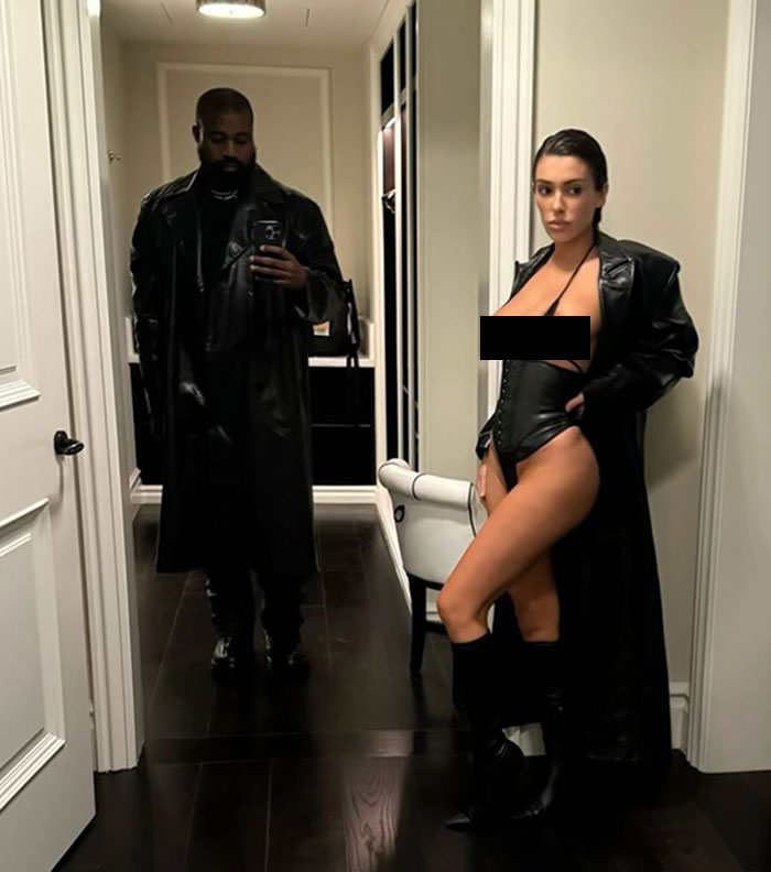 Kanye West taking mirror selfie while Bianca Censori poses in sheer nightie and leather coat in hallway. Kanye West taking mirror selfie while Bianca Censori poses in sheer nightie and leather coat in hallway.