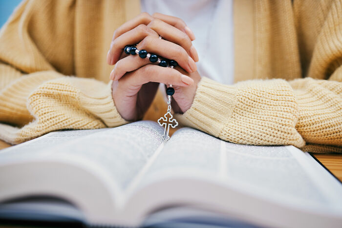 Person holding rosary beads over an open book, illustrating normal people's habits some netizens find creepy. - 16