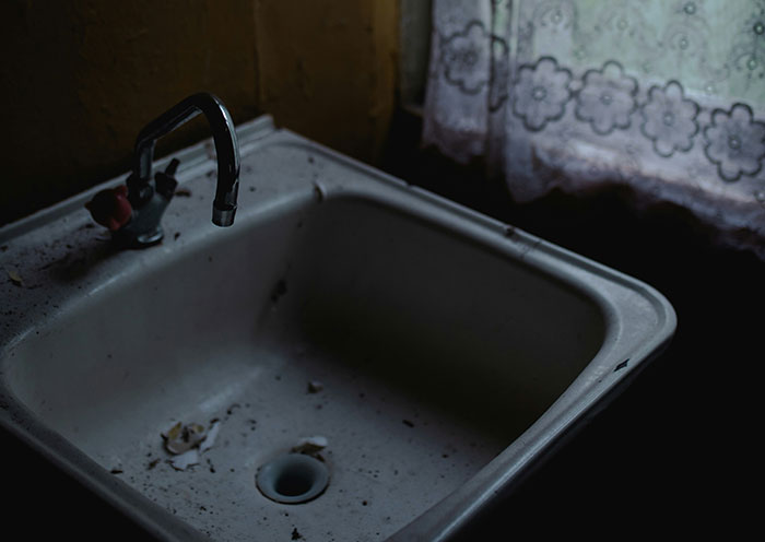 Dirty old sink with dark stains under a floral curtain, highlighting home red flags that turn a first date into a last one