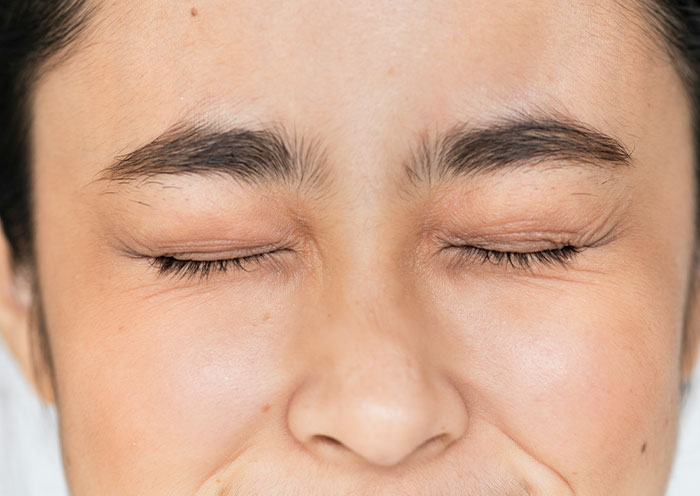 Close-up of a person's face with eyes tightly closed, expressing discomfort or disgust related to home red flags on a first date.
