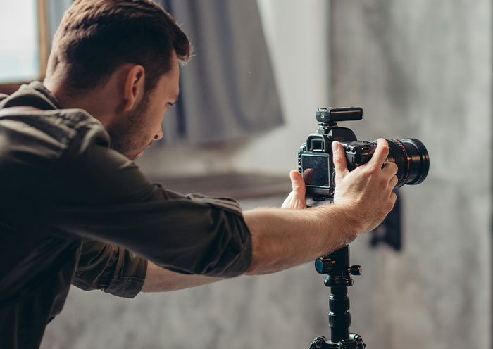 Man adjusting camera on tripod indoors, illustrating home red flags that turn a first date into a last one.