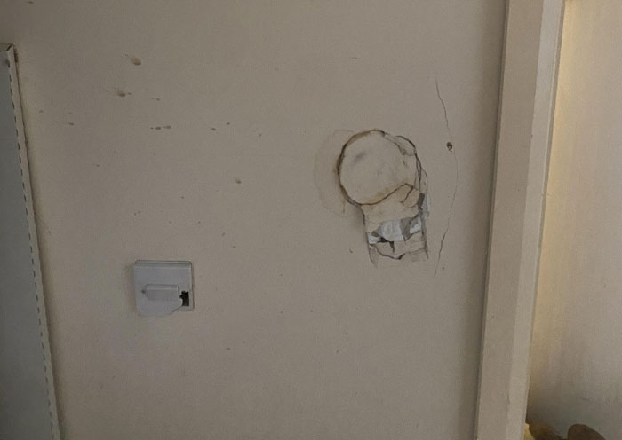 Wall with visible home red flags such as damaged paint and a broken outlet in a dated interior setting.