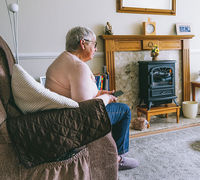 Elderly woman sitting in a living room with a fireplace, reflecting on a family home and related disputes. - 16
