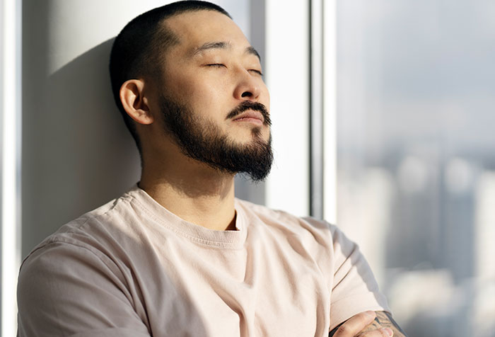 Man with beard and closed eyes reflecting by window, symbolizing conflict over wife’s childhood home and family demands. - 23